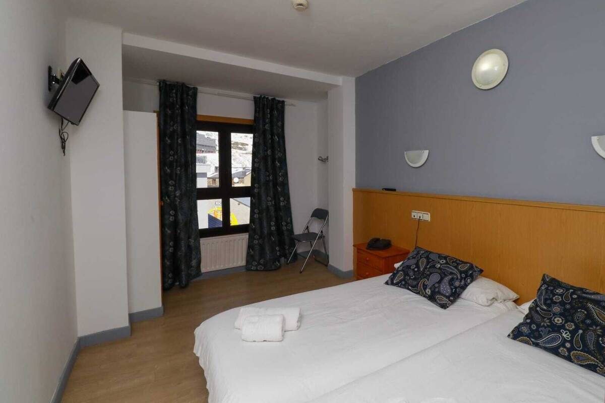 Een hotelkamer met een bed, een aan de muur bevestigde televisie, een raam met gordijnen en een radiator.