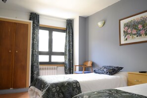 Een slaapkamer met twee bedden, een houten garderobe, een stoel, een nachtkastje en een raam met gordijnen.