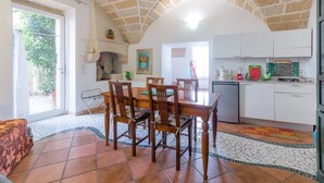 Un coin repas avec une table et des chaises en bois, une cuisine avec des meubles blancs et un sol carrelé.