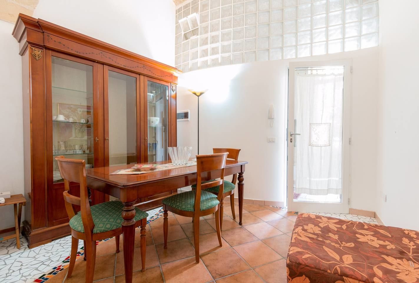 A dining area with a wooden table and chairs, a cabinet with glass doors, and a patterned rug.