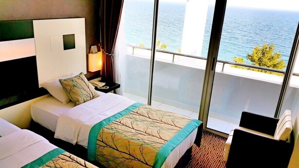 A hotel room with two beds, a nightstand, a lamp, and a view of the sea. - Blue Garden Hotel (Konyaalti)