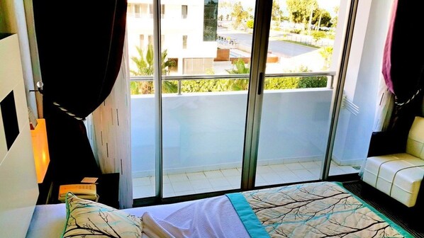A bedroom with a bed, a window with curtains, a view of the outside, and a balcony. - Blue Garden Hotel (Konyaalti)