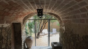 An arched doorway leading to an outdoor area with a large vase, a bench, and a hanging light fixture. - Hostal Can Xicu (Capmany)