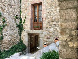 Un edificio de piedra con un balcón de madera, una pequeña entrada y macetas con plantas.