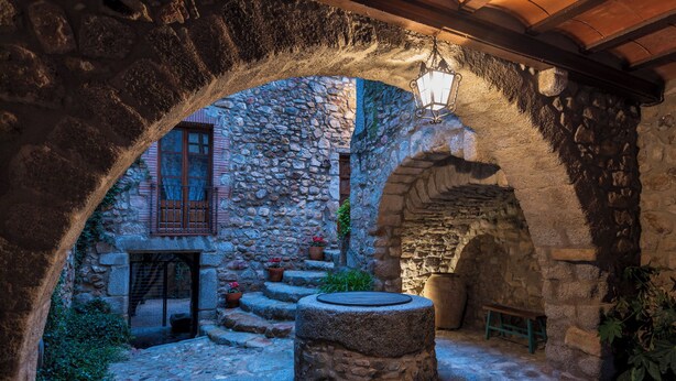 An outdoor courtyard with stone walls, a wooden bench, and a hanging light fixture. - Hostal Can Xicu (Capmany)