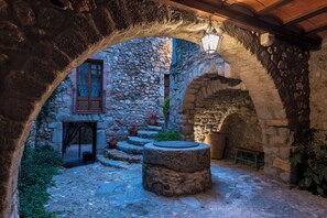 An outdoor courtyard with stone walls, a wooden bench, and a hanging light fixture. - Hostal Can Xicu (Capmany)