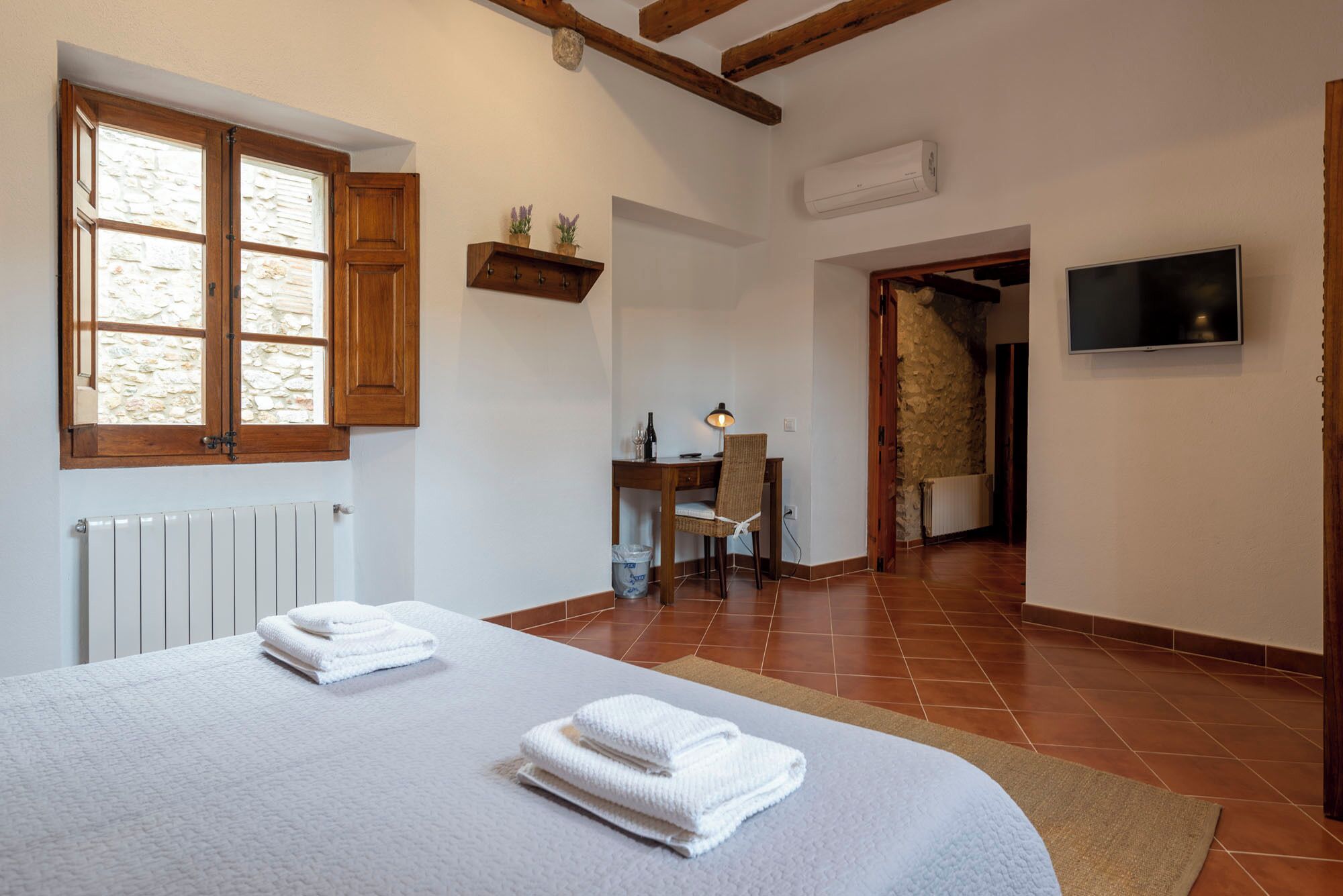 Un dormitorio con una cama, un escritorio, una silla, un televisor y una pared de piedra.