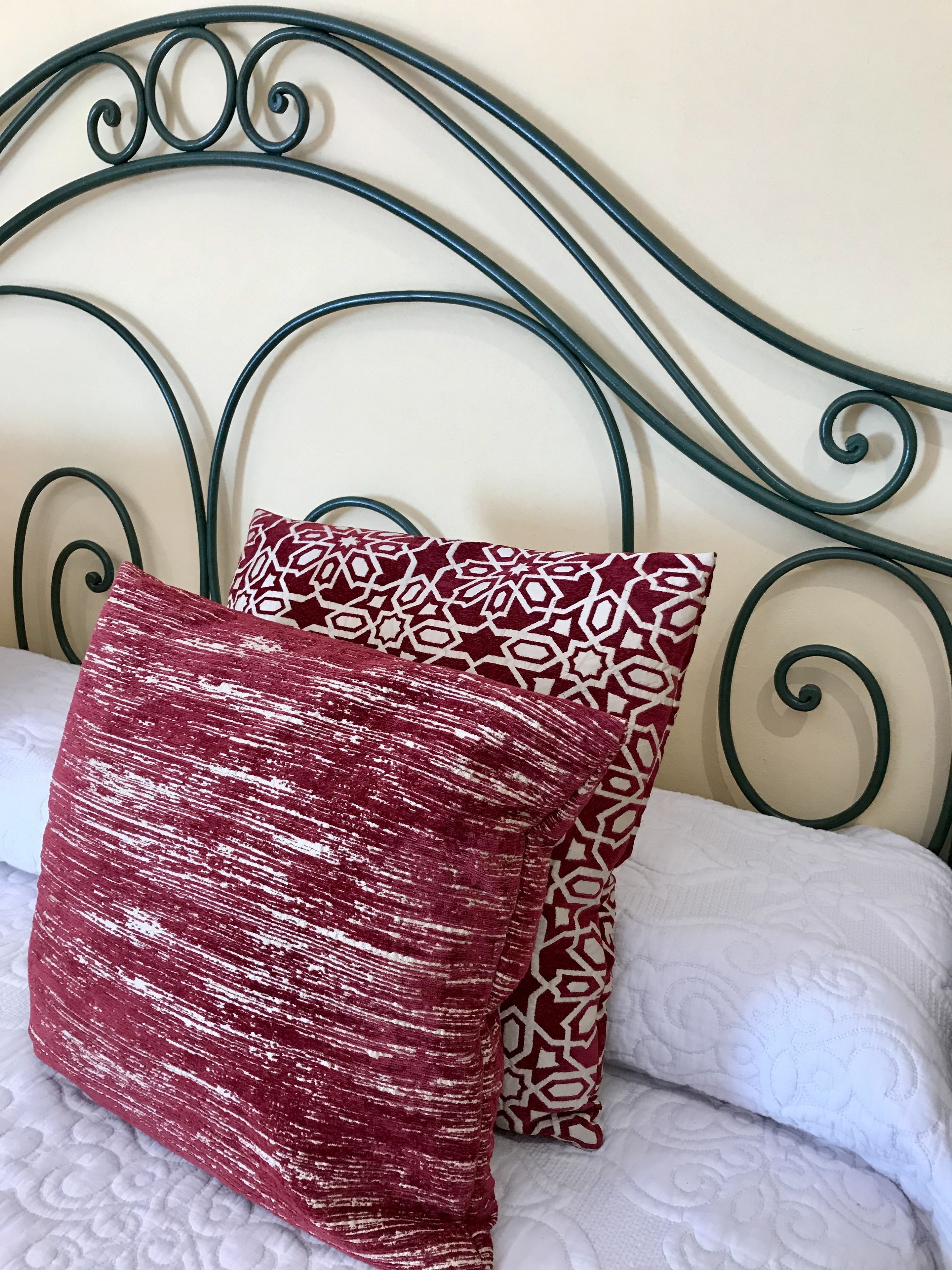 A bed with a metal headboard, two patterned pillows, and a white quilted bedspread.