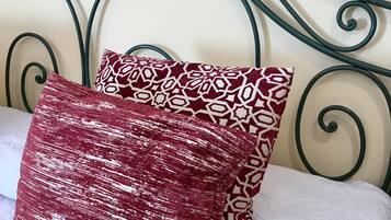 A bed with a metal headboard, two patterned pillows, and a white quilted bedspread.