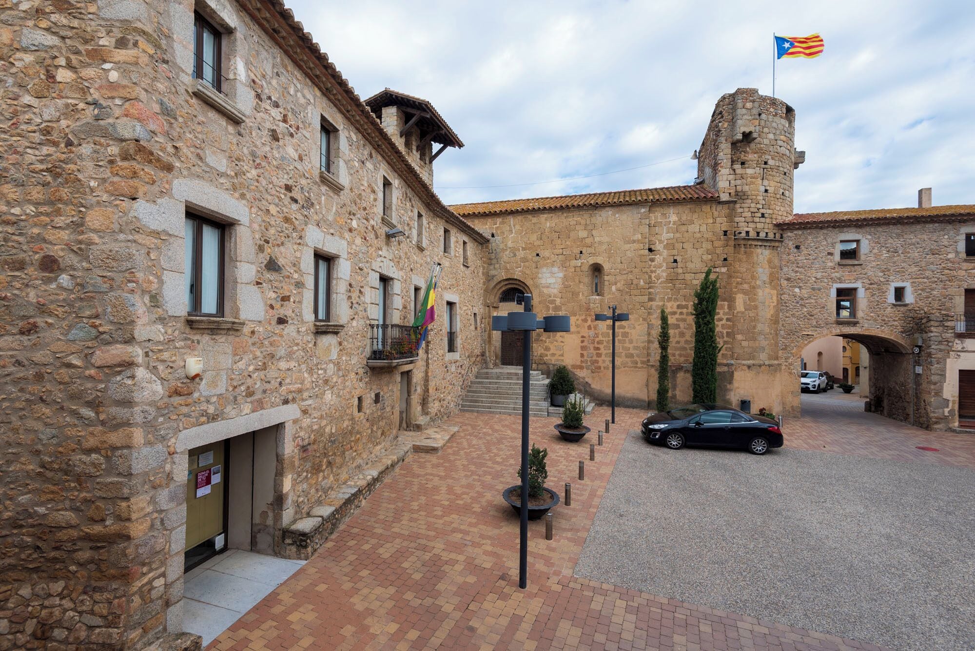 A stone building with a flag, a courtyard, and a car.