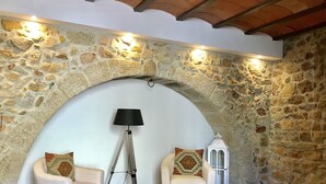A cozy room with a stone wall, two armchairs with patterned cushions, a floor lamp, and a white lantern. - Hostal Can Xicu (Capmany)