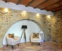 Un cuarto acogedor con pared de piedra, dos sillones con cojines estampados, una lámpara de pie y un farol blanco.