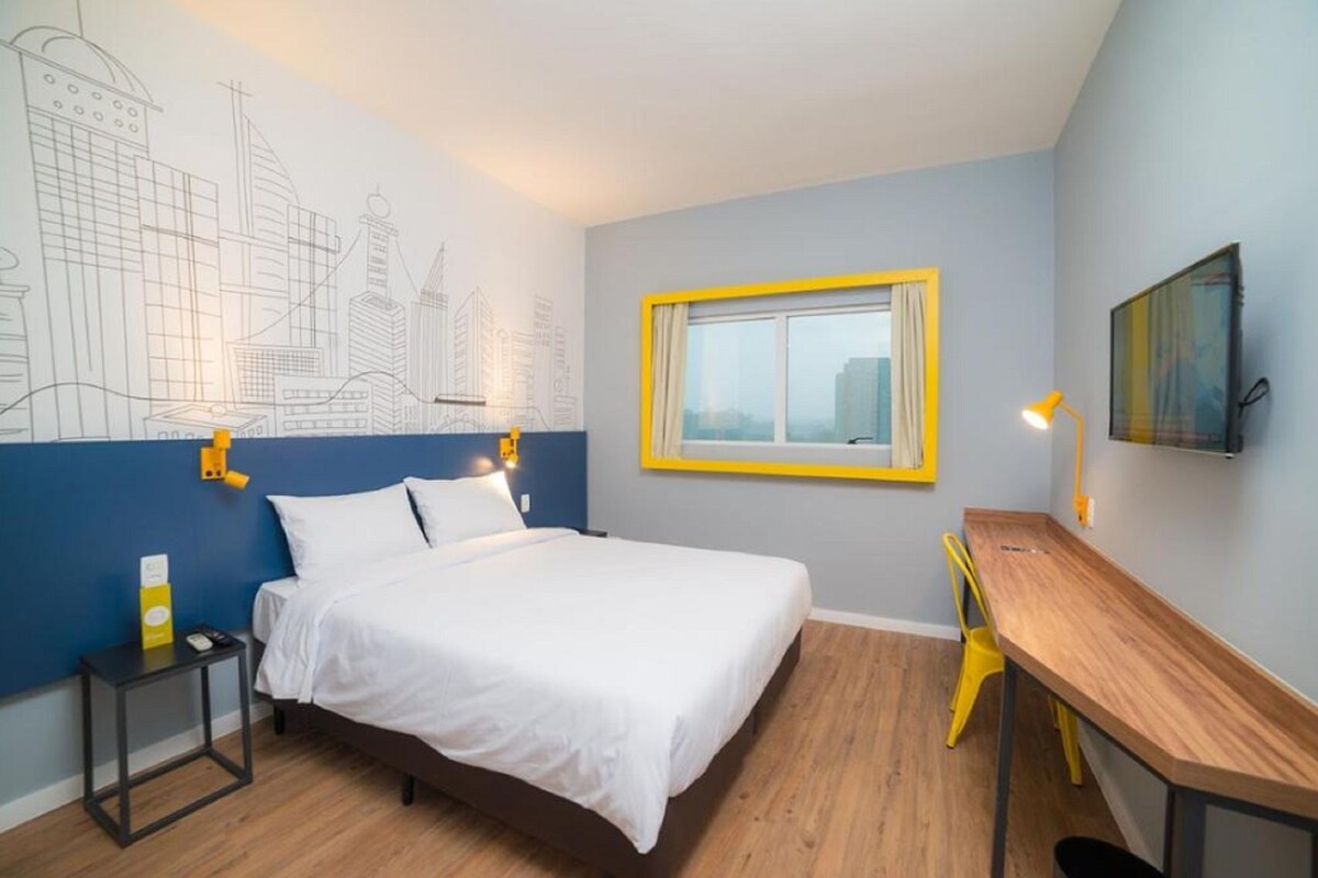 Ein Schlafzimmer mit Bett, Schreibtisch, Stuhl, Fenster und Wandbild.
