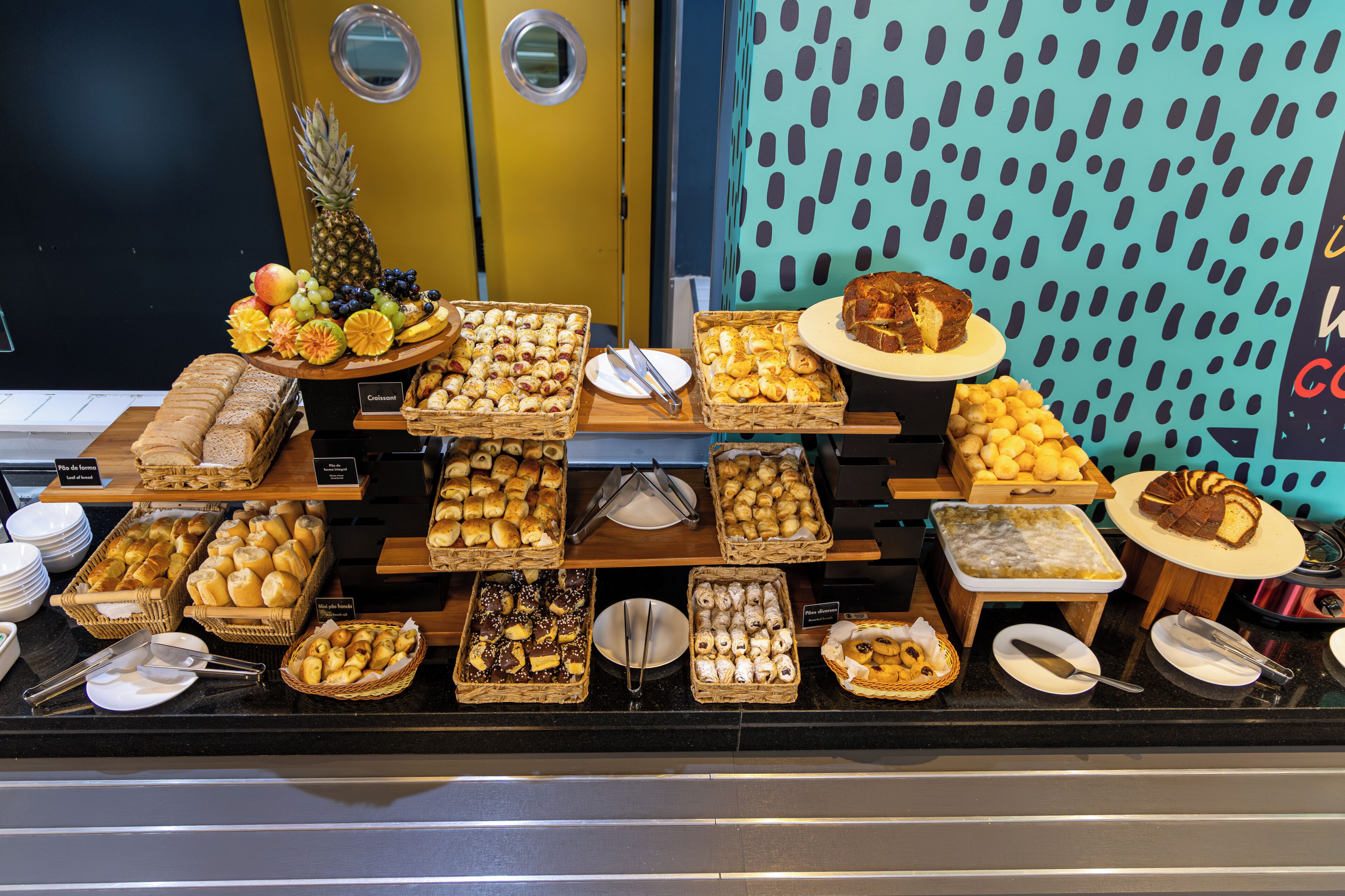 Buffet com diversos alimentos, incluindo pão, doces e frutas.