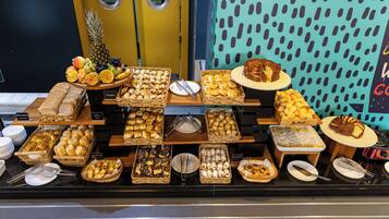 Buffet com diversos alimentos, incluindo pão, doces e frutas.