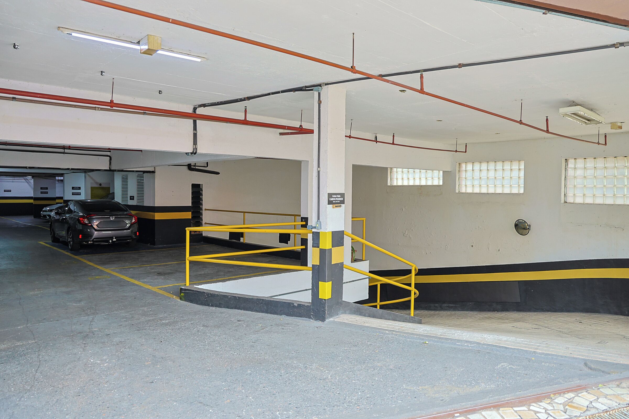 A parking garage with a yellow safety barrier, a car, and a stairwell.