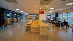 A spacious indoor area with a long wooden counter, seating arrangements, and large windows providing natural light. - B&B Hotels São José dos Campos (São José dos Campos)