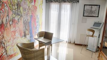 Una habitación con una mesa de vidrio, sillas de mimbre, una laptop, una balanza y un cuadro en la pared.