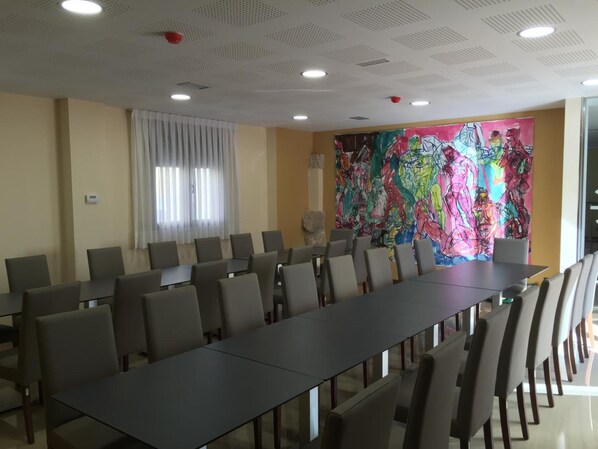 A conference room with a long table and chairs, a colorful abstract painting on the wall, and a window with blinds. - Hotel En El Camino (Boadilla del Camino)
