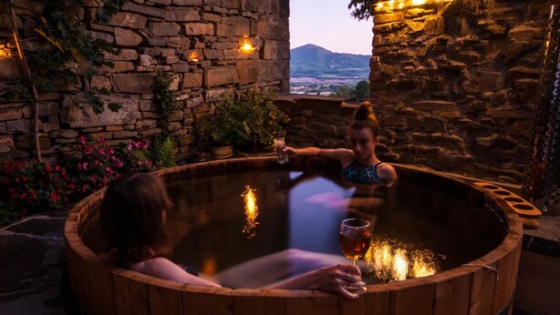 A wooden hot tub with two people sitting inside, surrounded by stone walls and potted plants. - O Chardinet d'a Formiga (La Fueva)