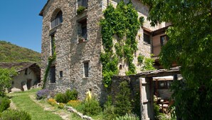 A stone building with multiple windows and balconies, surrounded by greenery and a clear sky. - O Chardinet d'a Formiga (La Fueva)