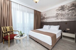 Ein Hotelzimmer mit einem großen Bett, einem Nachttisch, einem Sessel, einem kleinen Tisch mit Pflanze und einem Gemälde an der Wand.