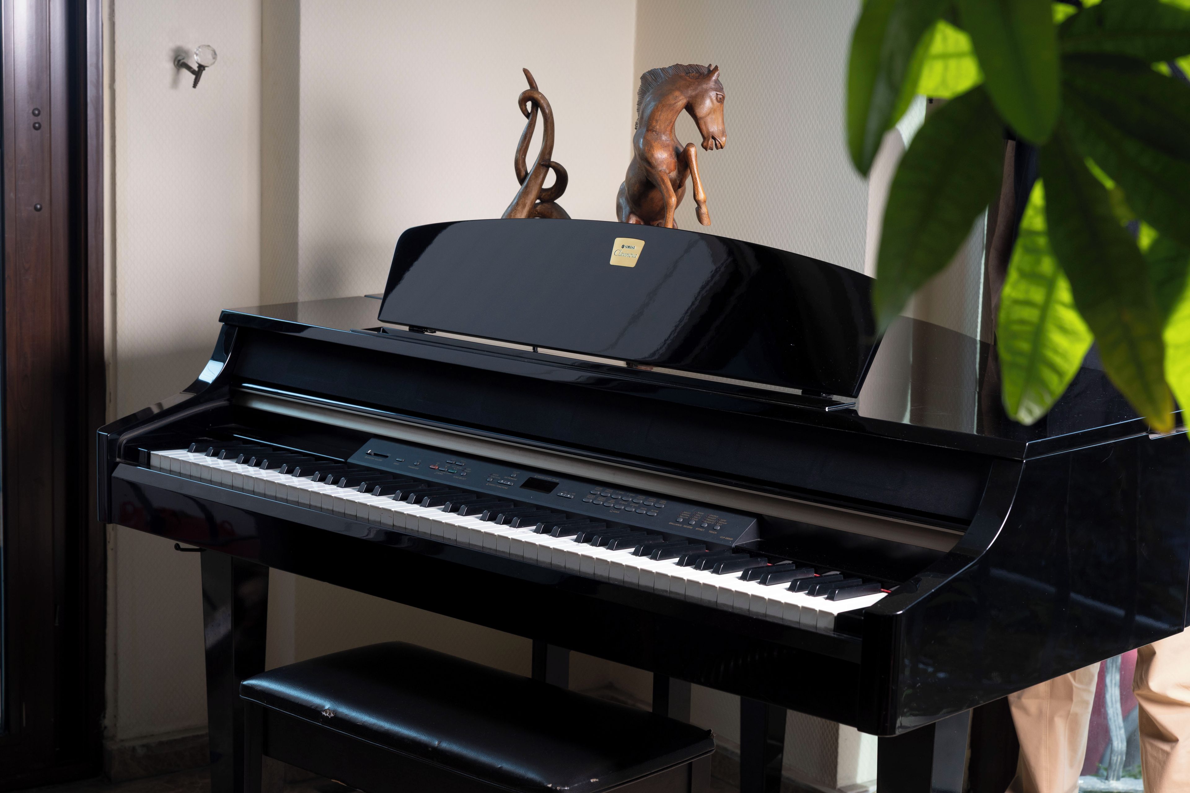 A piano with a bench in front of a wall with a decorative horse sculpture.