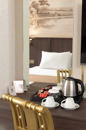 A hotel room with a dining table set for breakfast, including a kettle, cups, and a tray of pastries.