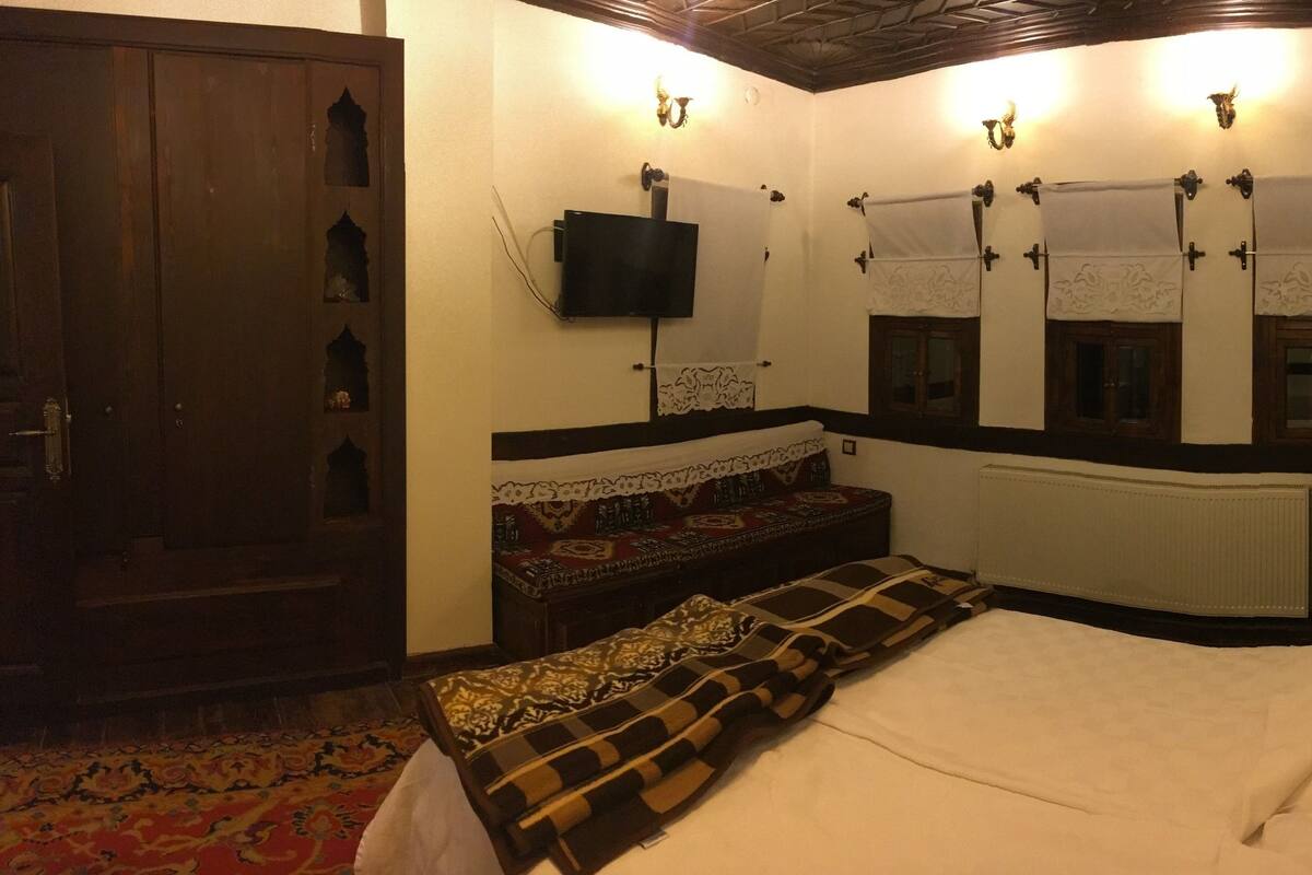 A traditional room with a bed, a bench, a television, and a radiator.