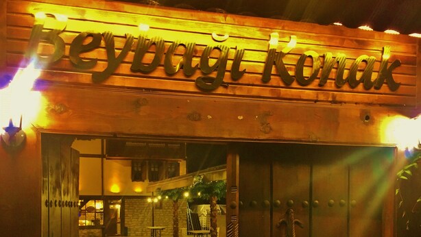 Una entrada de madera con el nombre "Beybuca Konak" iluminado en la parte superior.