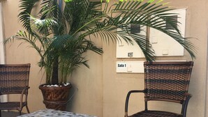 A patio area with two wicker chairs, a small table, and a large potted plant. - Trindade Hotel (Trindade)