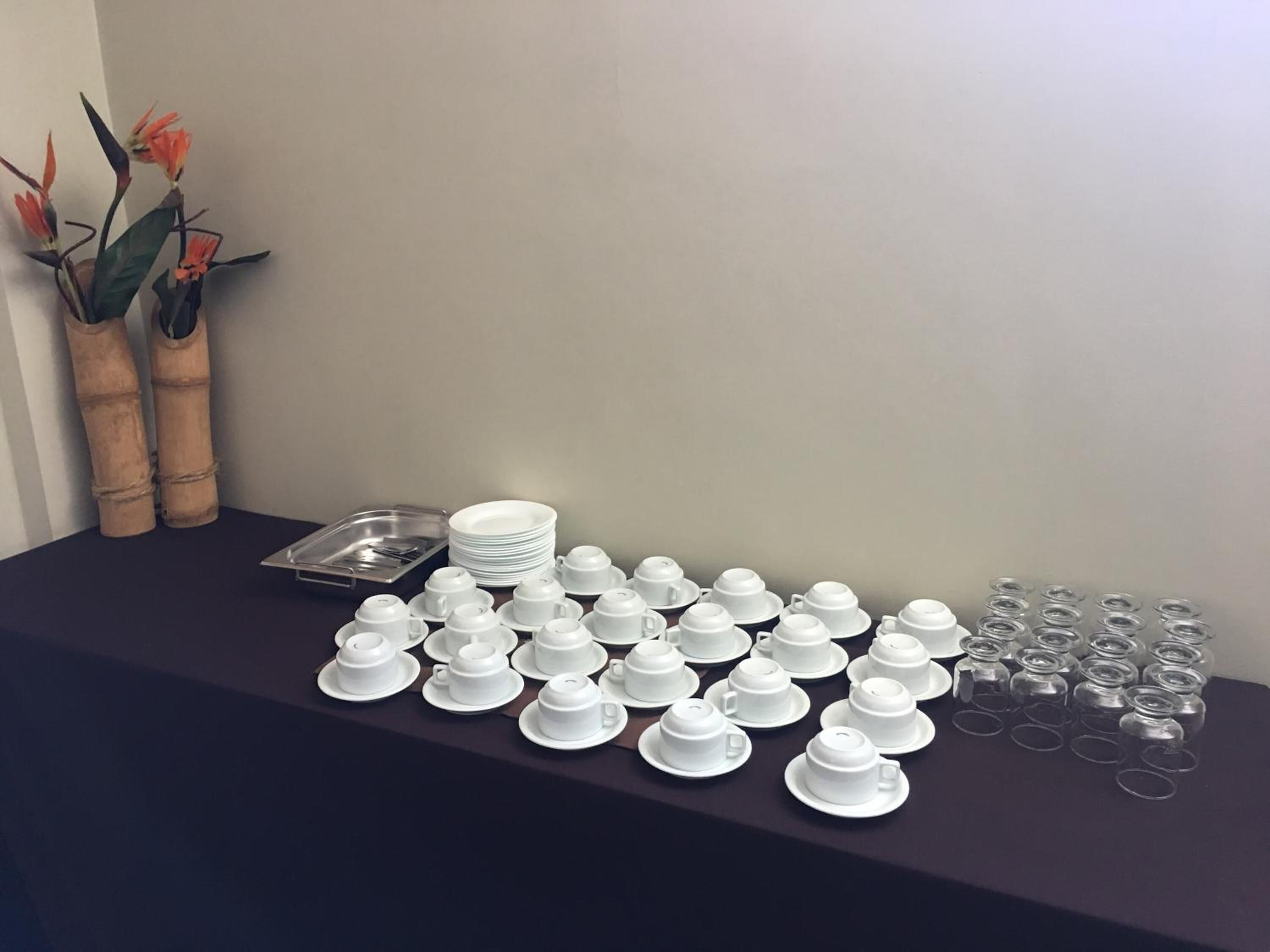 Een tafel met witte theekopjes, schoteltjes en een stapel witte borden.