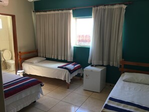 A small, clean room with two single beds, a small refrigerator, and a window with curtains. - Trindade Hotel (Trindade)