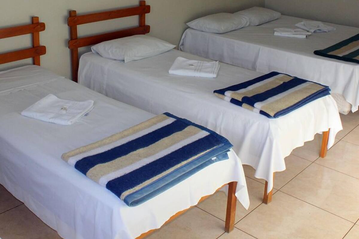 A hotel room with three single beds, each with a white bedspread and a blue-striped blanket.