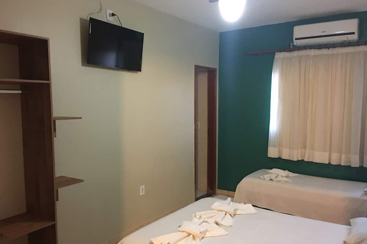 A hotel room with two beds, a television, an air conditioning unit, and a wardrobe.