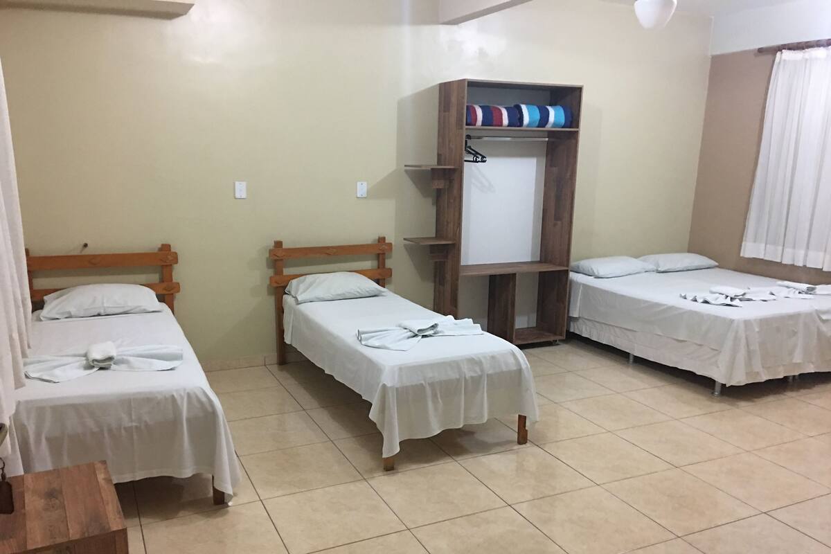 A hotel room with three single beds, a wooden wardrobe, and a tiled floor.