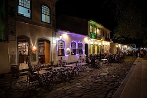 Un carrer pavimentat amb terrasses a un restaurant, finestres il·luminades i façana tradicional.
