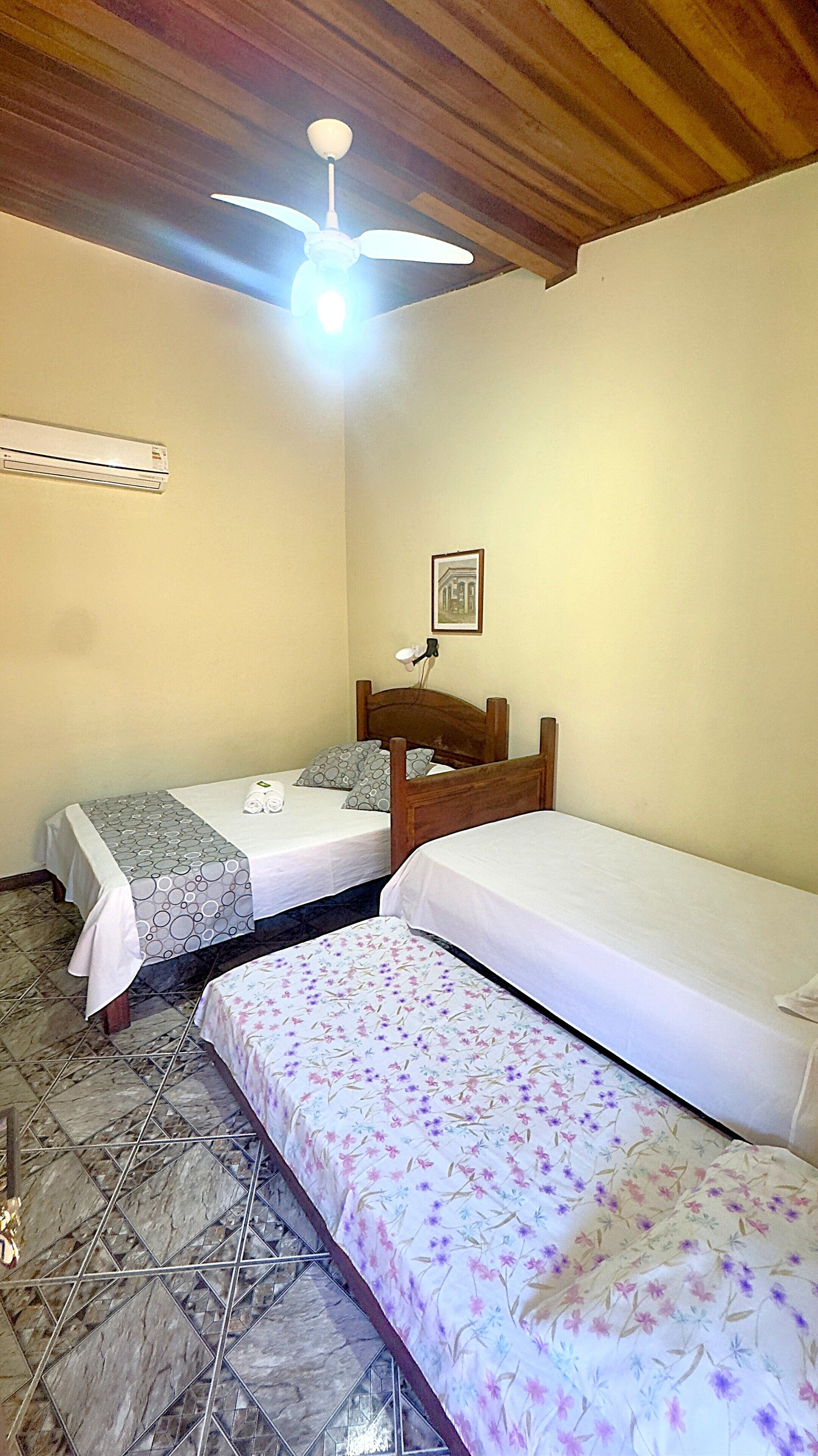 A room with two single beds, a ceiling fan, a wall-mounted air conditioner, and a framed picture on the wall.