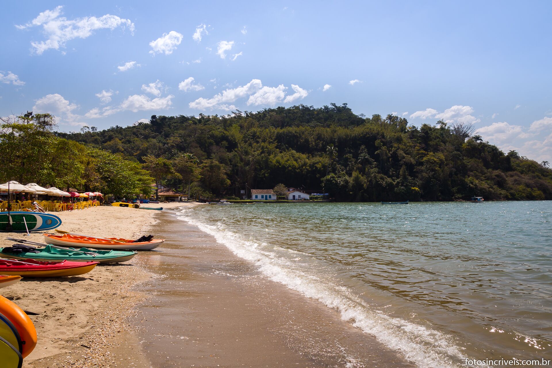A beach with kayaks, a sandy shore, and a forested hill in the background.