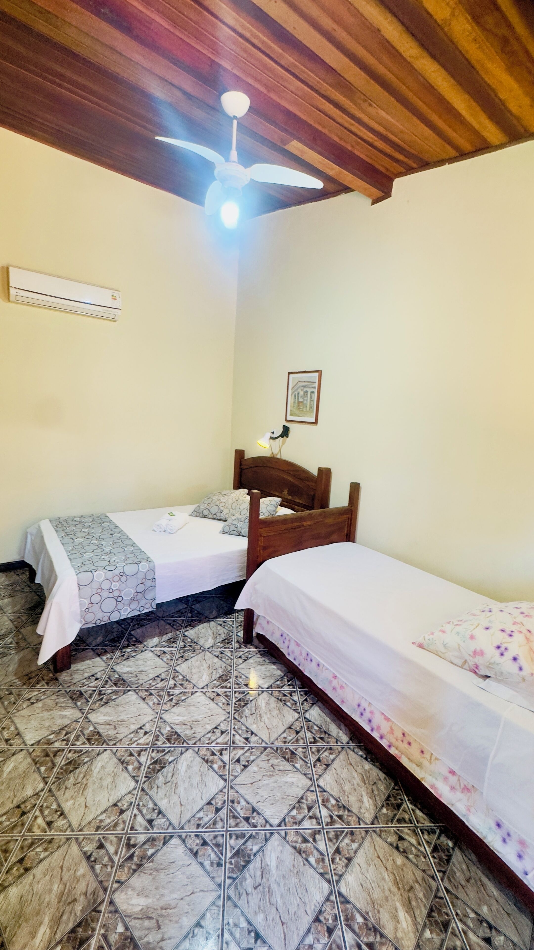 Une chambre avec deux lits simples, un ventilateur de plafond, un climatiseur mural et un sol carrelé.