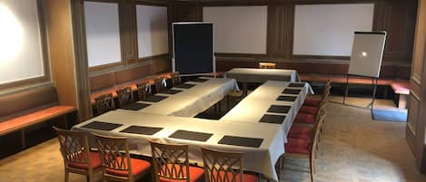 A conference room with long tables, chairs, and a projector screen.