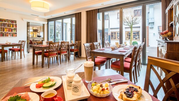 A dining area with tables, chairs, and a variety of food items. - Weinstadt-Hotel (Weinstadt)