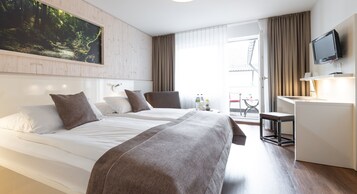 Une chambre d’hôtel avec deux lits, un bureau, une télévision et une grande fenêtre avec des rideaux.