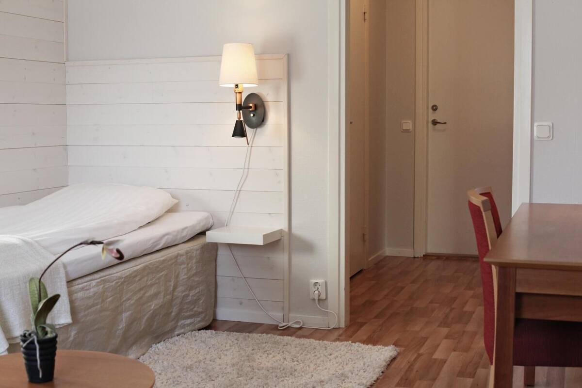 Een slaapkamer met een bed, nachtkastje, lamp en een kleine plant in een pot.