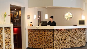 A reception desk with a unique log wall design, a round mirror, and a bar area visible in the background. - Sorsele River Hotel (Sorsele)