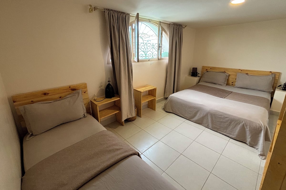 A room with two beds, a small table, a nightstand, and a window with curtains.