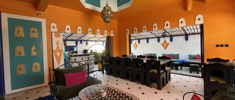 A room with orange walls, a patterned floor, and a central seating area with a table and chairs.