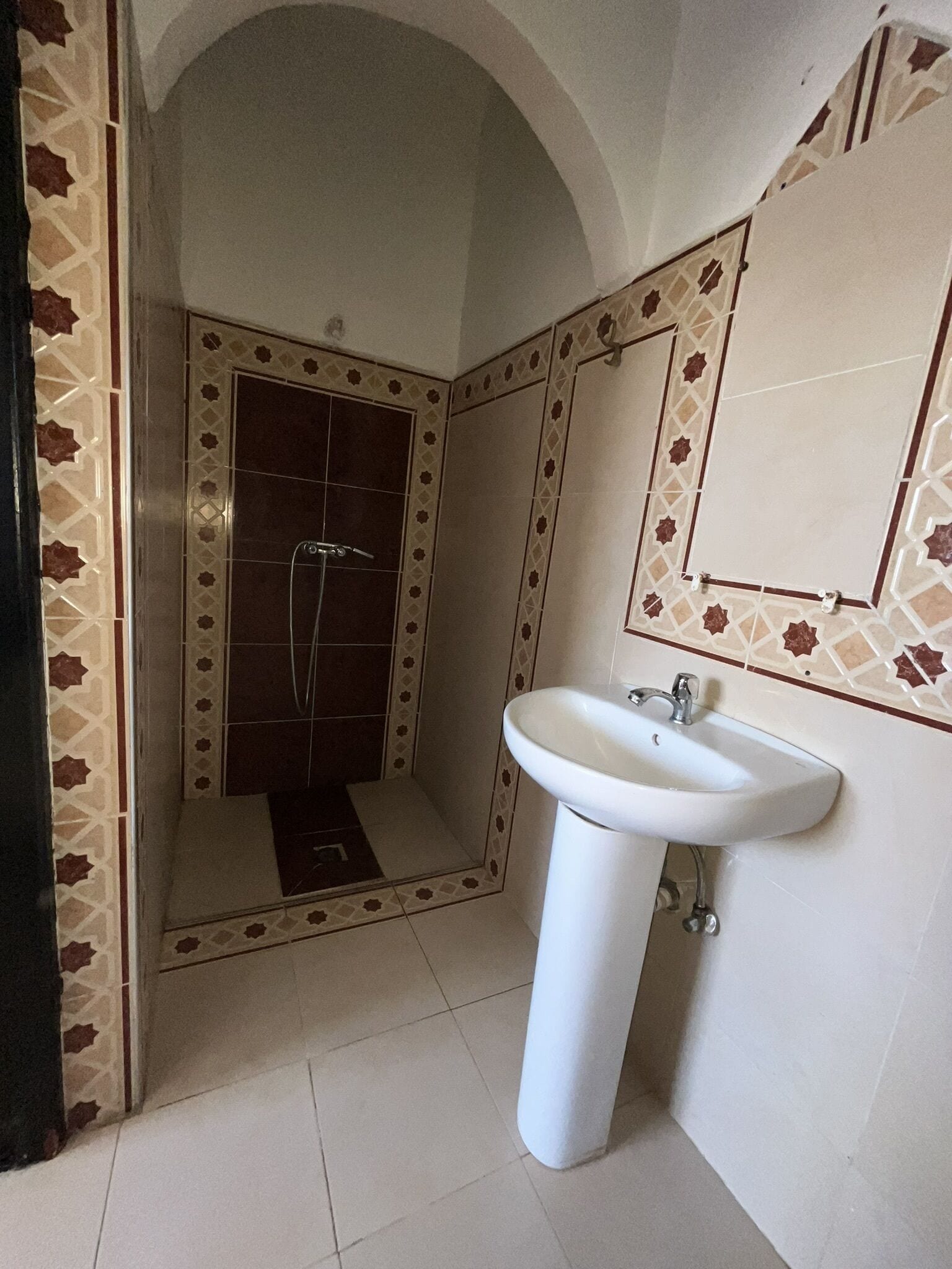 A bathroom with a white sink, a shower, and patterned tiles.