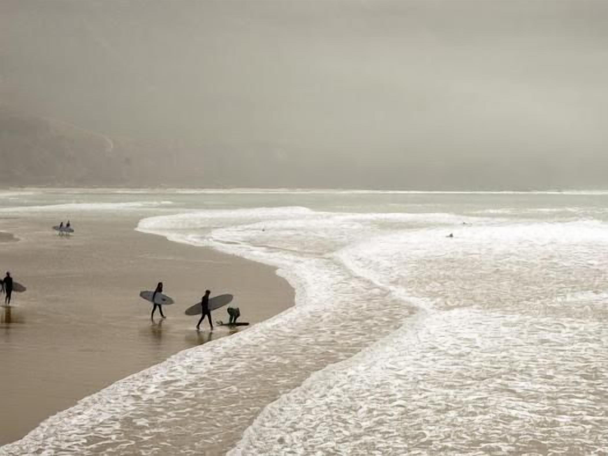 Een strand met golven en mensen die met surfplanken lopen.