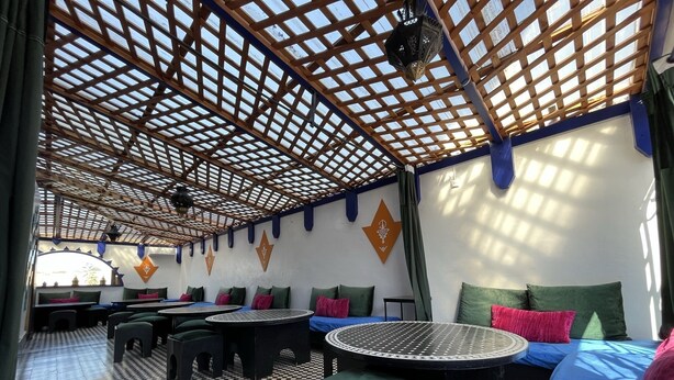 A covered outdoor seating area with tables and chairs, patterned flooring, and decorative wall elements. - Riad Dar Naima Imsouane (Imsouane)